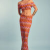 Colorful retro two-piece outfit with wavy pink, orange, and yellow pattern, featuring an off-shoulder crop top and matching skirt with cutout details
