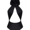 This is a stylish black halter-neck one-piece swimsuit with a unique design featuring a dramatic, voluminous ruffle at the chest, creating a floral or layered effect. The swimsuit has a cut-out detail under the ruffle, exposing part of the torso in a subtle yet elegant way. The material looks sleek and slightly glossy, enhancing the sophistication of the piece.
